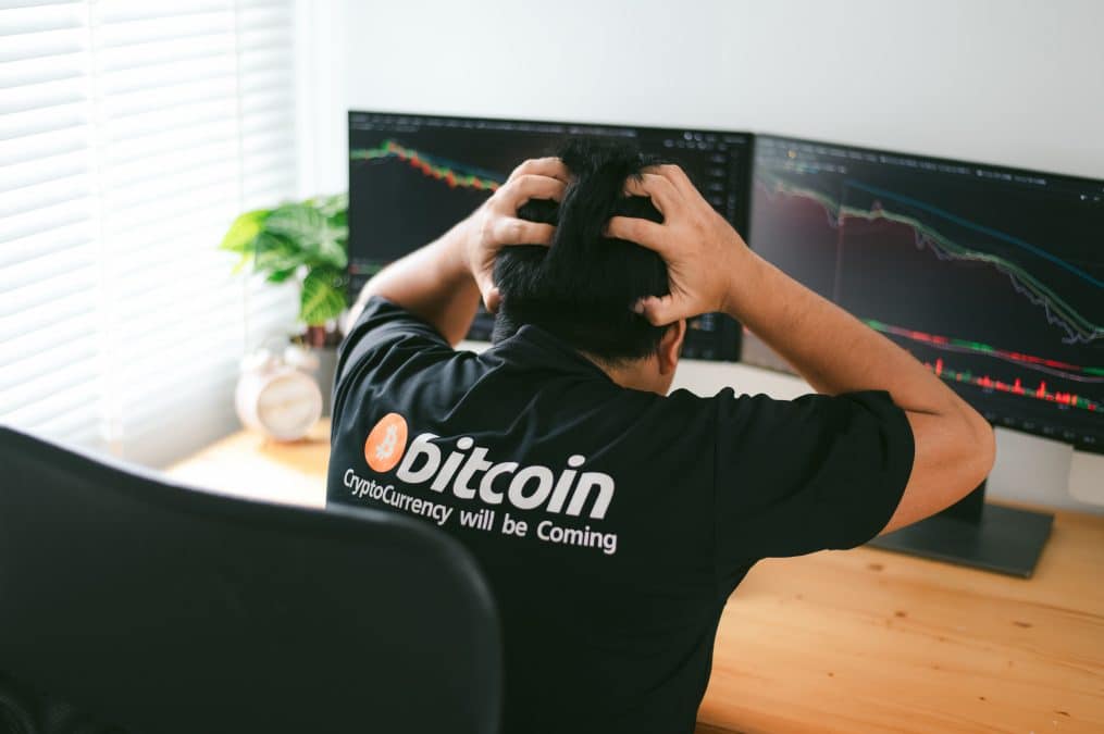 Homem com camisa do Bitcoin desesperado olhando gráfico de preço