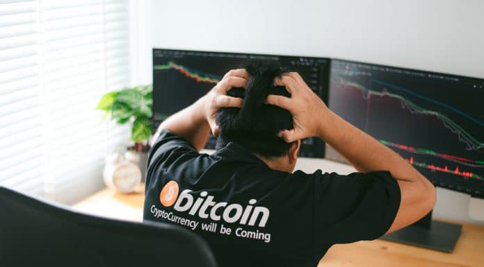 Homem com camisa do Bitcoin desesperado olhando gráfico de preço