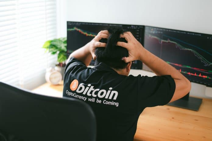 Homem com camisa do Bitcoin desesperado olhando gráfico de preço