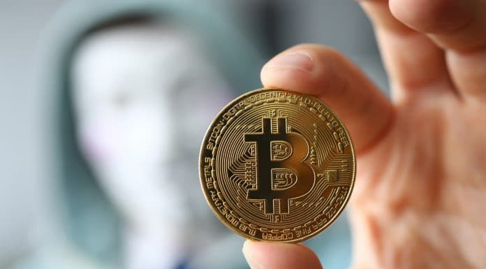 Hacker usando máscara e segurando Bitcoin desconhecido