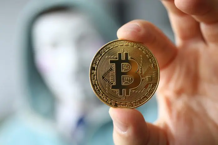 Hacker usando máscara e segurando Bitcoin desconhecido