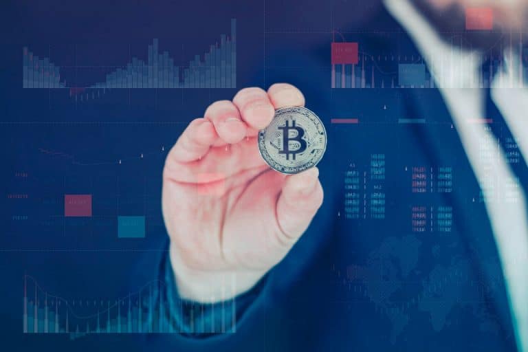 Mão segurando Bitcoin em gráficos de mercado