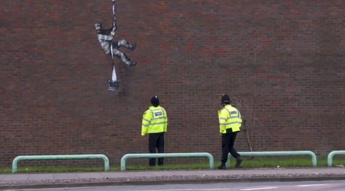 Obra pública do Banksy sendo observada por policiais