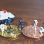 Polícia em Miniatura investigando uma moeda física de Bitcoin