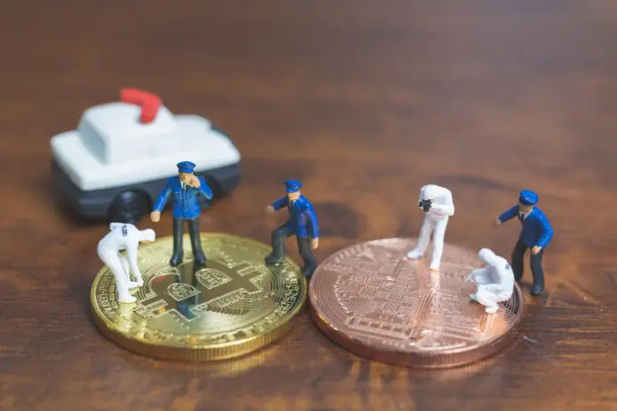 Polícia em Miniatura investigando uma moeda física de Bitcoin