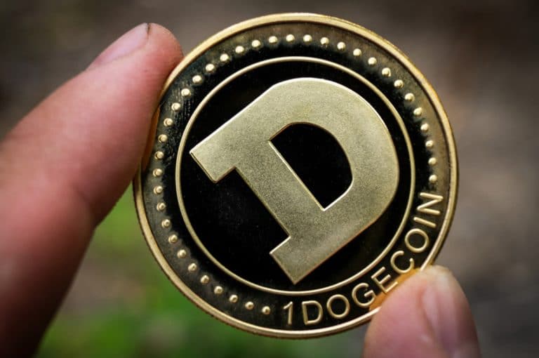 Um dogecoin físico segurado por dedos