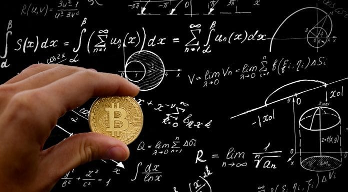Mão segurando Bitcoin em frente a lousa com fórmulas matemáticas