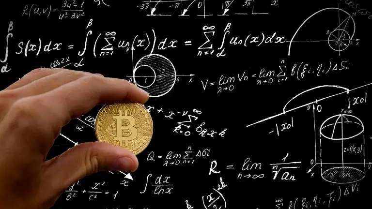 Mão segurando Bitcoin em frente a lousa com fórmulas matemáticas