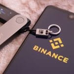 Aplicativo da corretora Binance ao lado de uma carteira ledger
