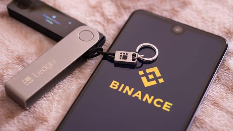 Aplicativo da corretora Binance ao lado de uma carteira ledger
