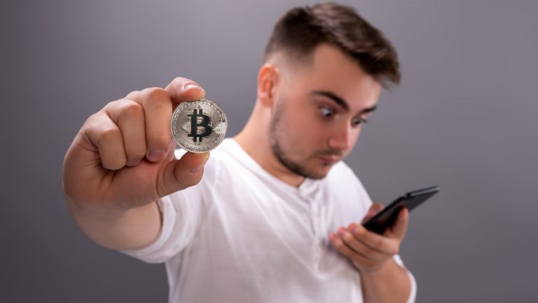 Homem jovem olhando para celular e segurando um Bitcoin criptomoedas FIRE