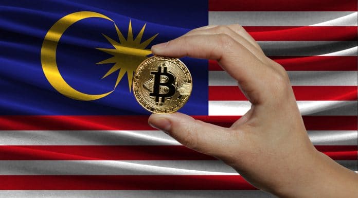Mão segurando Bitcoin e bandeira da Malásia
