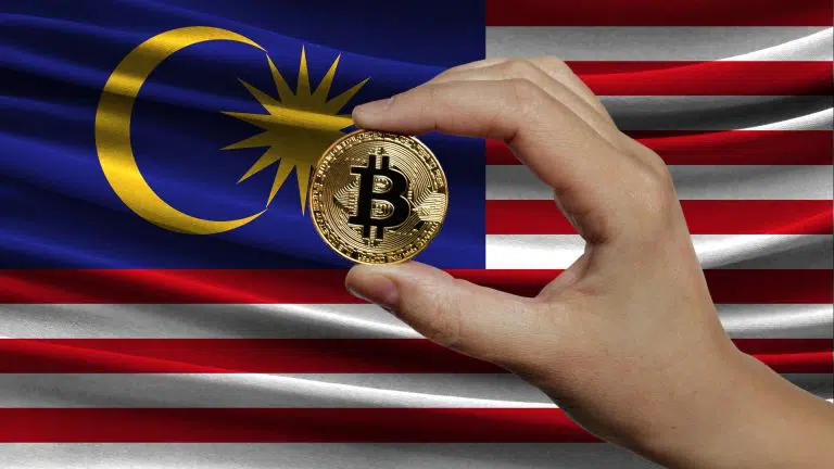 Mão segurando Bitcoin e bandeira da Malásia