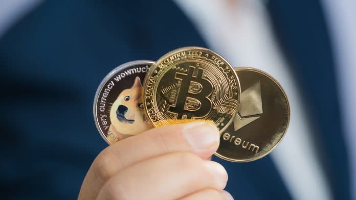 Mão segurando criptomoedas Bitcoin, Ethereum e Dogecoin