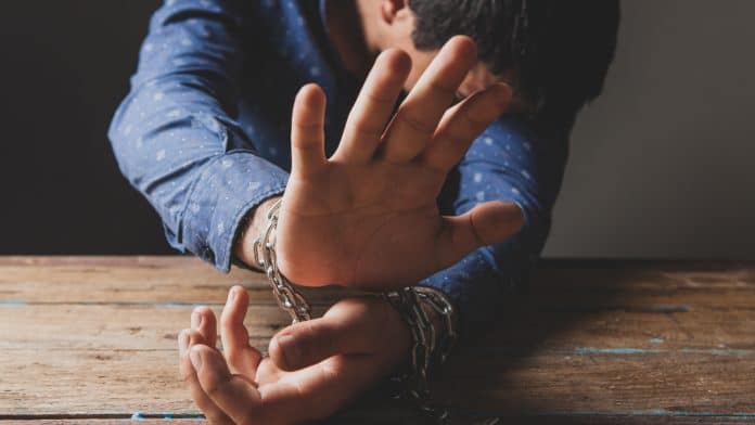 Homem preso cobrindo o rosto criptomoedas golpe Bitcoin fraude condenado