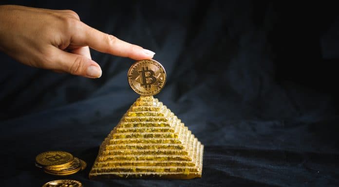 Mão segurando Bitcoin no topo de pirâmide líder