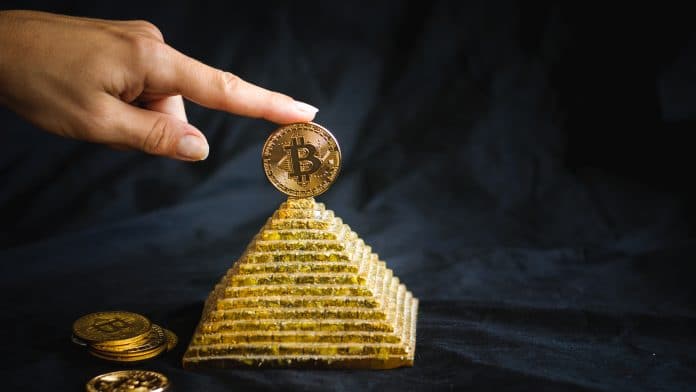 Mão segurando Bitcoin no topo de pirâmide líder