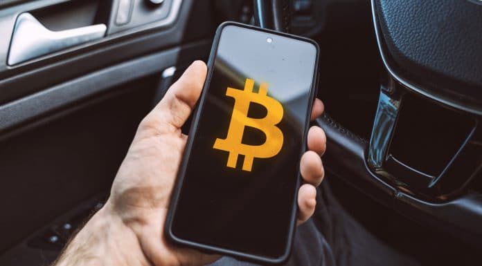 Aplicativo de Bitcoin é segurado por pessoa sentada em um carro estacionamento