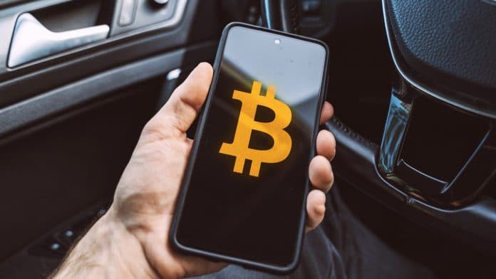 Aplicativo de Bitcoin é segurado por pessoa sentada em um carro estacionamento