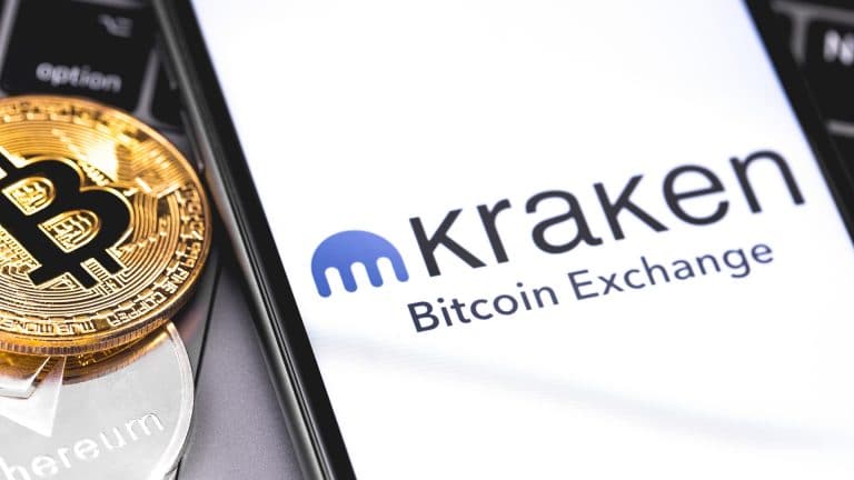 Celular com aplicativo da corretora Kraken ao lado de moeda do Bitcoin