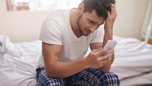 Homem mexendo em celular e sentado na cama estudante perdendo