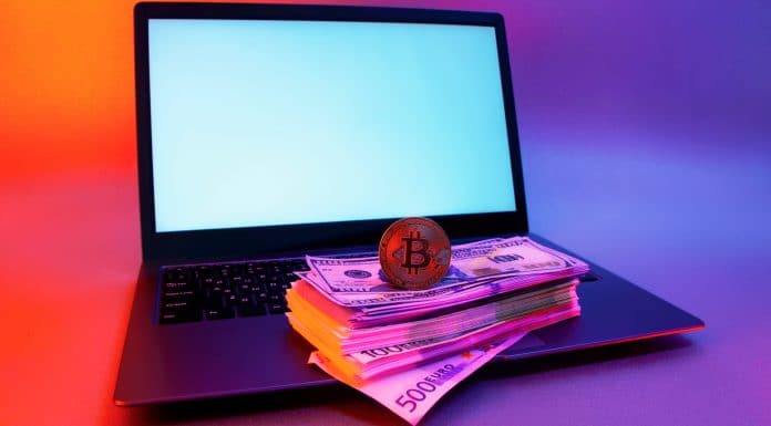 Notebook com pilha de dinheiro e Bitcoin em cima ransomwares