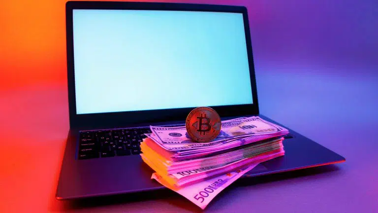 Notebook com pilha de dinheiro e Bitcoin em cima ransomwares