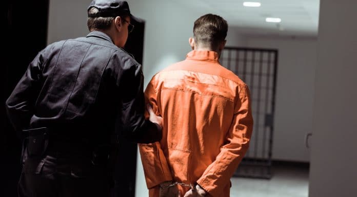 Homem sendo preso com roupa laranja por policial