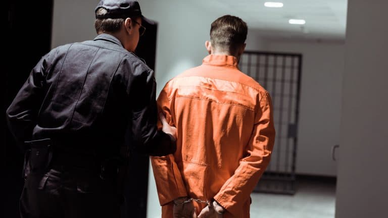 Homem sendo preso com roupa laranja por policial