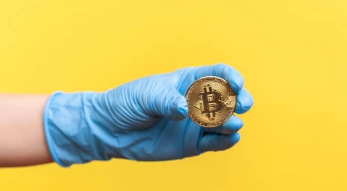 Mão com luva cirurgica segurando Bitcoin