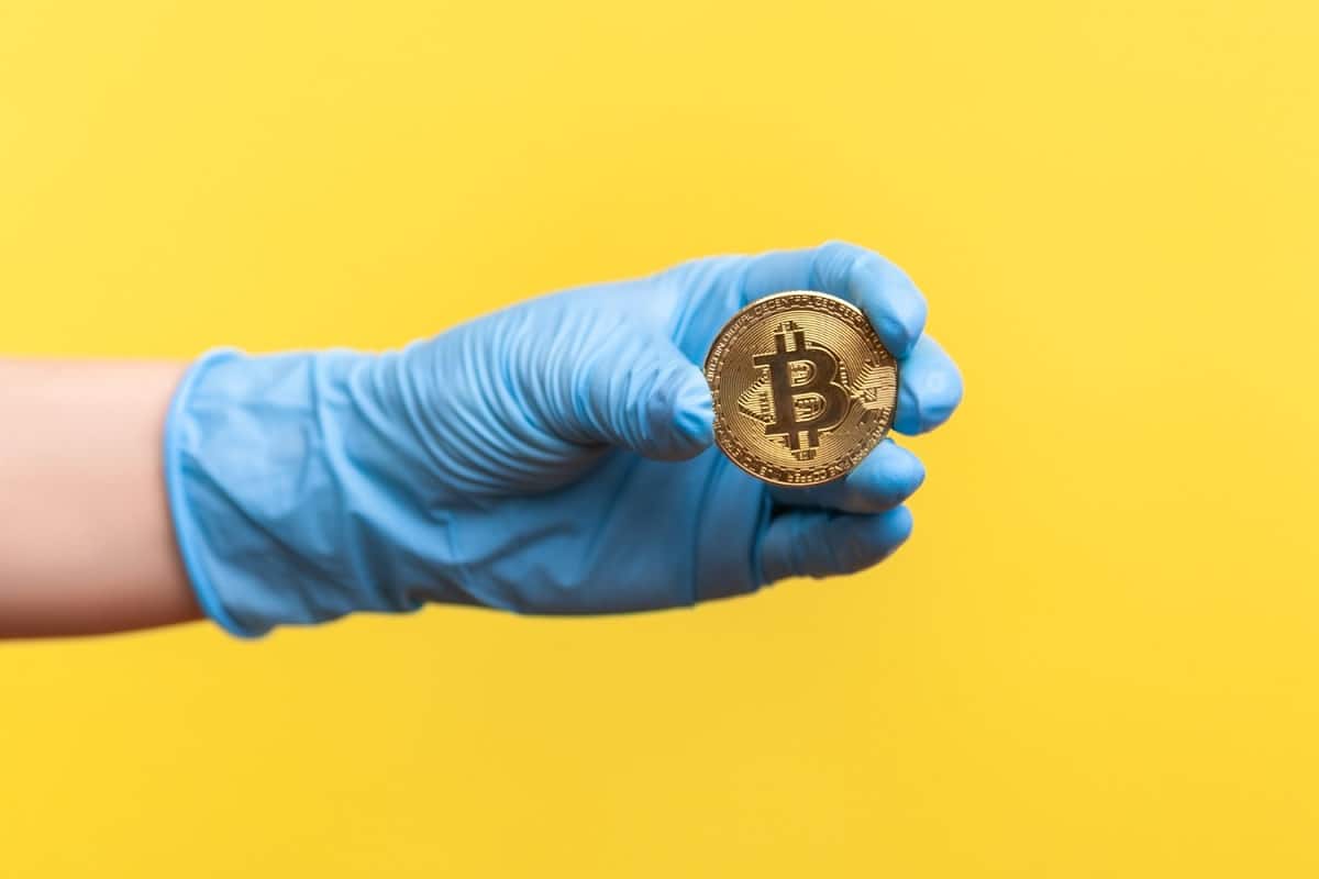 Mão com luva cirurgica segurando Bitcoin