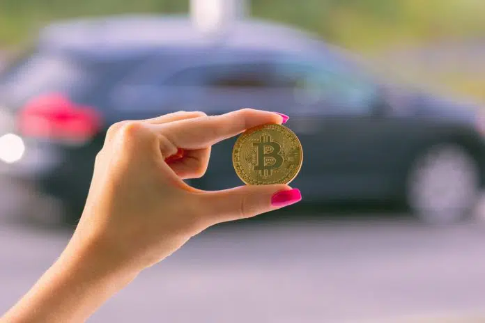Mão de mulher segurando Bitcoin próximo a um carro