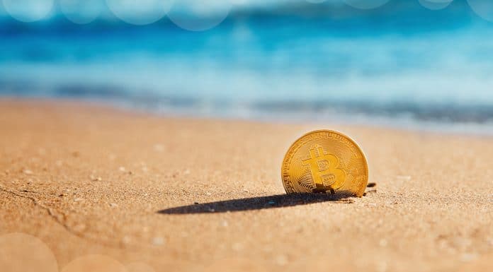 Moeda Bitcoin parcialmente enterrada na areia da praia