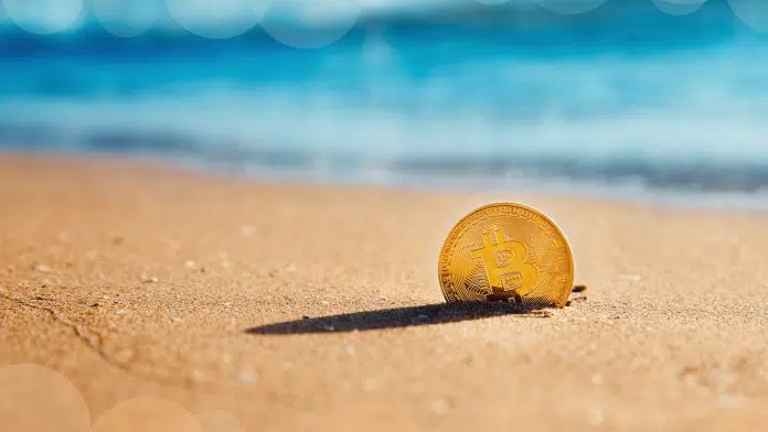 Moeda Bitcoin parcialmente enterrada na areia da praia