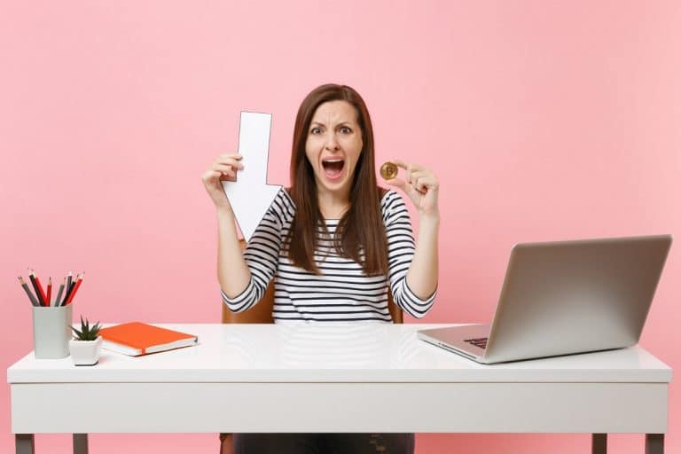 Mulher com medo ao segurar Bitcoin em queda