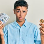 Homem cético segurando dólares e Bitcoin
