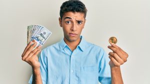 Homem cético segurando dólares e Bitcoin