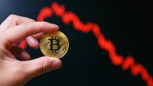 Mão segurando Bitcoin e gráfico de preços em queda