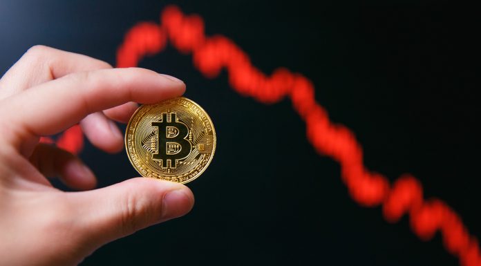 Mão segurando Bitcoin e gráfico de preços em queda