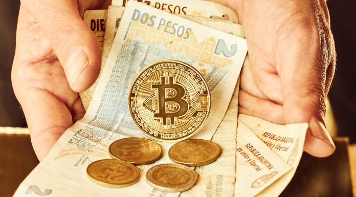 Mão segurando cédulas e moedas da Argentina e Bitcoin