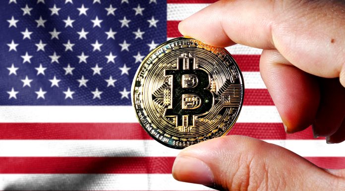Mão segurando o Bitcoin em frente a bandeira dos Estados Unidos
