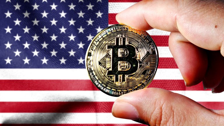 Mão segurando o Bitcoin em frente a bandeira dos Estados Unidos