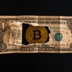 Uma nota de um dólar rasgada através da qual as moedas Bitcoin são visíveis