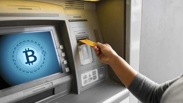 Mão de uma mulher inserindo o cartão do banco na máquina ATM com o ícone do bitcoin na tela
