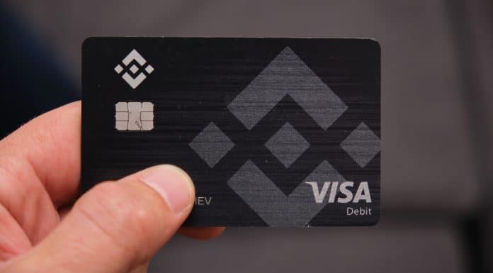 Mão segura o cartão de débito Binance, bandeira Visa