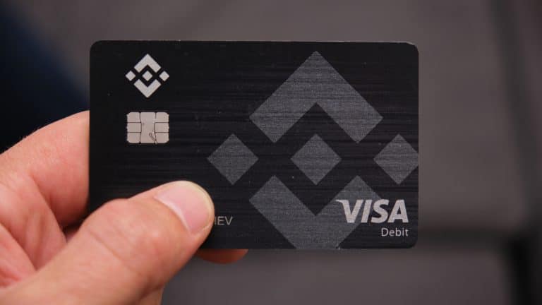 Mão segura o cartão de débito Binance, bandeira Visa