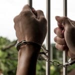 Mãos algemadas de prisioneiro masculino na cadeia
