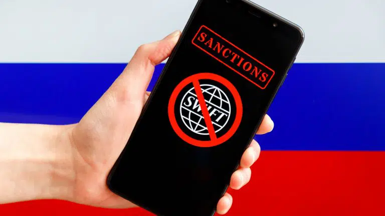Celular com bandeira do SWIFT em sanção com bandeira da Rússia ao fundo