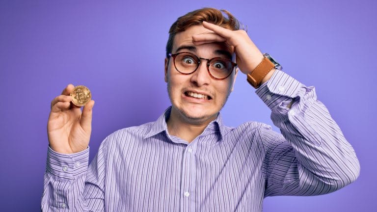 Jovem segurando Bitcoin com expressão engraçada de arrependimento