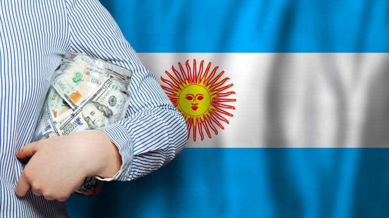 Mão segurando notas próximo a bandeira da Argentina